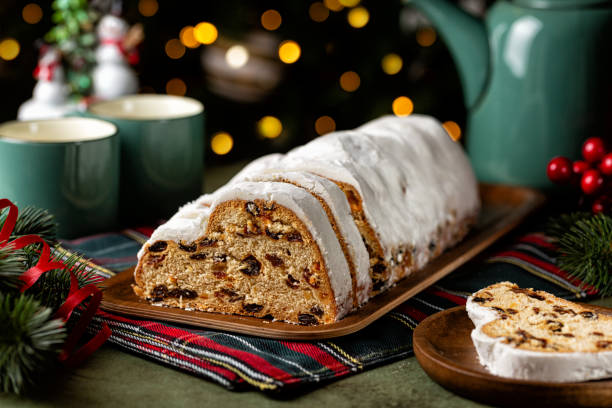 istock Served table with Stollen cake, tea cups and pot. German Christmas dessert, bread chock full of dried fruit, candied peel, and almonds. Festive lights, tree and decoration. 2175690596