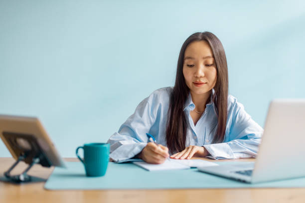 Diligent woman takes notes at desk with laptop on.