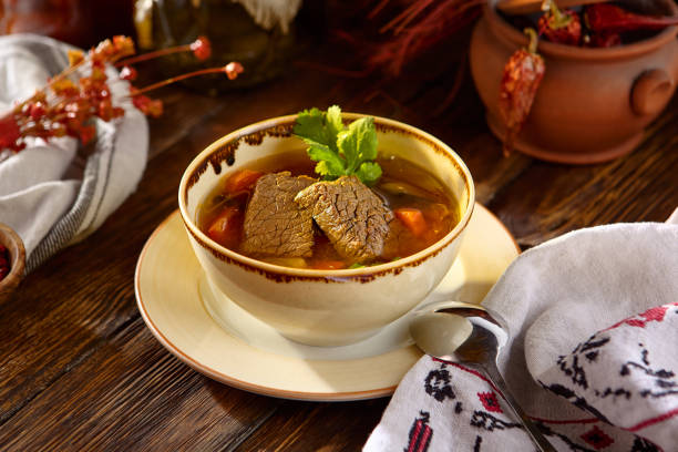 A close-up, high-angle shot of a white plate containing a traditional stew, likely Carne con Papas y Guisantes (Meat with Potatoes and Peas). The dish features chunks of cooked meat, yellow potato pieces, and green peas in a savory, orange-colored broth. Ideal for themes of global cuisine, comfort food, recipes, traditional cooking, and Latin American or Spanish food blogs/cookbooks.