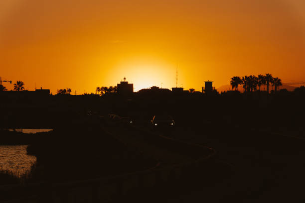 A stunning silhouette of a city skyline set against a vibrant orange sunset. The image captures the peaceful and tranquil essence of dusk with silhouetted buildings and palm trees.