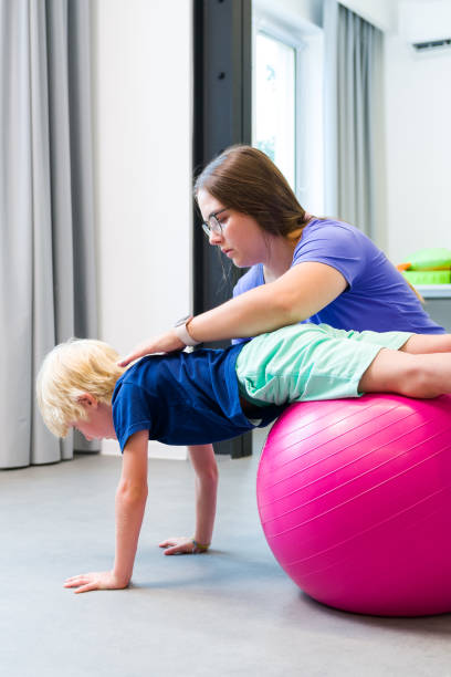 istock Young boy with female physical therapist exercising using ball during therapy session. Child physical therapy. Bilateral coordination. 2175693484