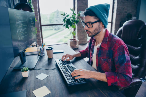 istock Photo of intelligent serious guy dressed eyewear typing code modern device keyboard indoors workstation workshop home 2175705604