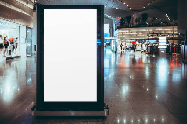 Blank white banner in shopping mall Blank digital advertising screen mockup in a modern airport terminal. Vertical billboard ready for branding, product promotion, or commercial use. Surrounded by retail stores and glossy floor retail digital signage stock pictures, royalty-free photos & images