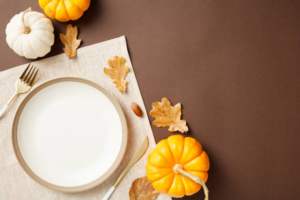 istock Autumn table setting featuring a white plate on a tablecloth with pumpkins, leaves, and golden cutlery. Perfect for festive designs, seasonal menus, and Thanksgiving celebrations 2175733979
