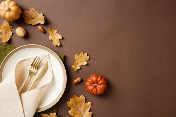 istock Thanksgiving dinner concept. Autumn table setting with elegant white dinnerware and golden cutlery amidst vibrant fall leaves and pumpkins. 2175734181