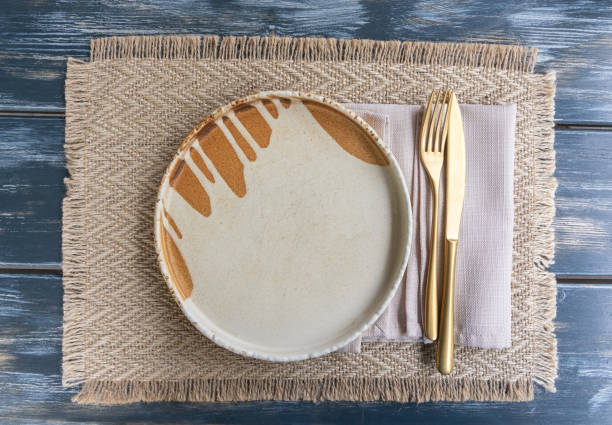 Empty restaurant plate mockup, rustic dark wood table setting with a white plate, a beige napkin and burlap placemat, farmhouse style dinner