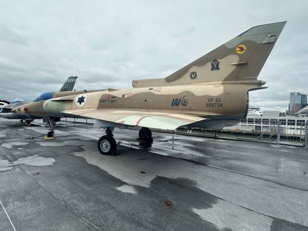 A retired F-4 Phantom fighter jet is showcased at a waterfront venue. The aircraft's unique camouflage paint and markings catch the eye