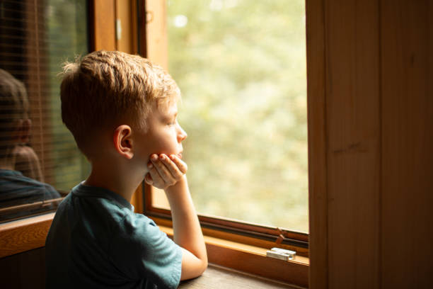 istock Thoughtful alone child at home looking out his window. 2175758479