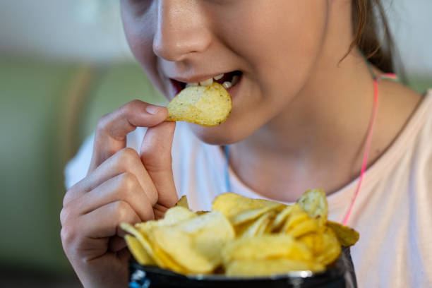 istock chips. Appealing young lady opening mouth and putting chip inside 2175763992