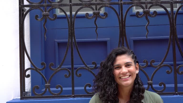 Smiling Woman Posing Against Blue Window with Decorative Ironwork
