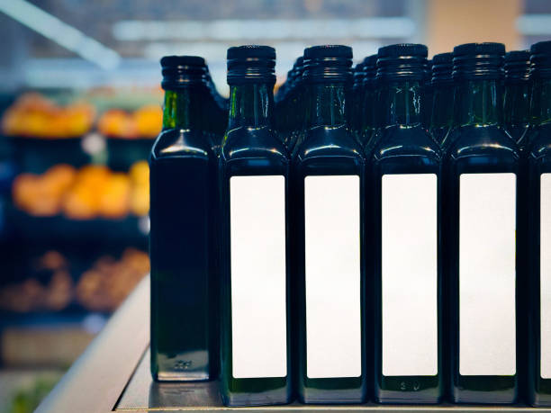 A row of dark green olive oil bottles displayed on a supermarket shelf with blank labels.