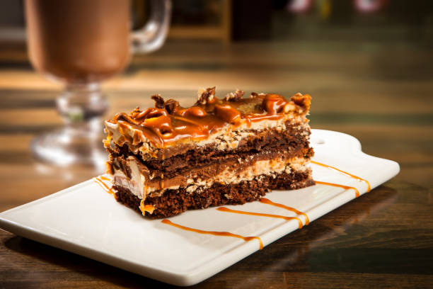 Decadent Chocolate Caramel Layer Cake with Drizzle Chocolate Sauce and Hot Chocolate Coffee mug served in tray dish isolated on table side view of cafe baked dessert food