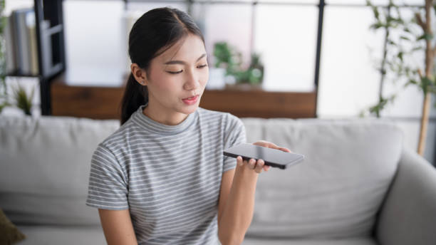 Asian woman using voice assistant on smartphone at home conversation with online assistantÂ Voice chat bot conversational AI Modern Technologies.