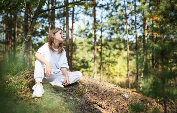 istock Young girl enjoying a sunny day in a forest clearing while sitting on a grassy mound surrounded by trees and nature 2175805795