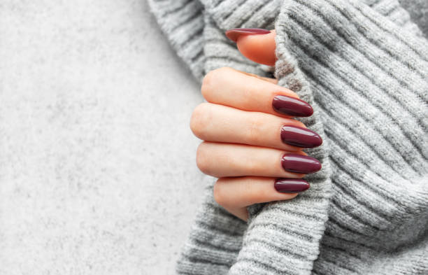 istock Elegant hand with deep red manicure holding a cozy gray sweater against a textured background in a softly lit setting 2175806101