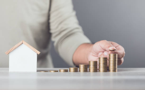 istock Man is stacking coins on a table, arranging them from smallest to largest, with a wooden house model beside him. Emphasizes the concept of saving money for future investments and financial stability 2175808237