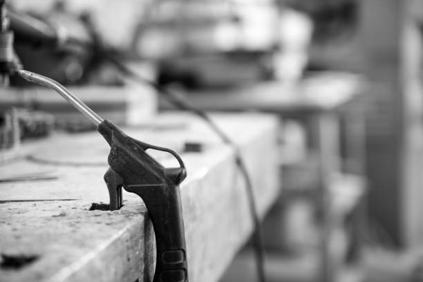 Black and white image of An air blow gun is resting on a workbench in a workshop, with tools and equipment visible in the background