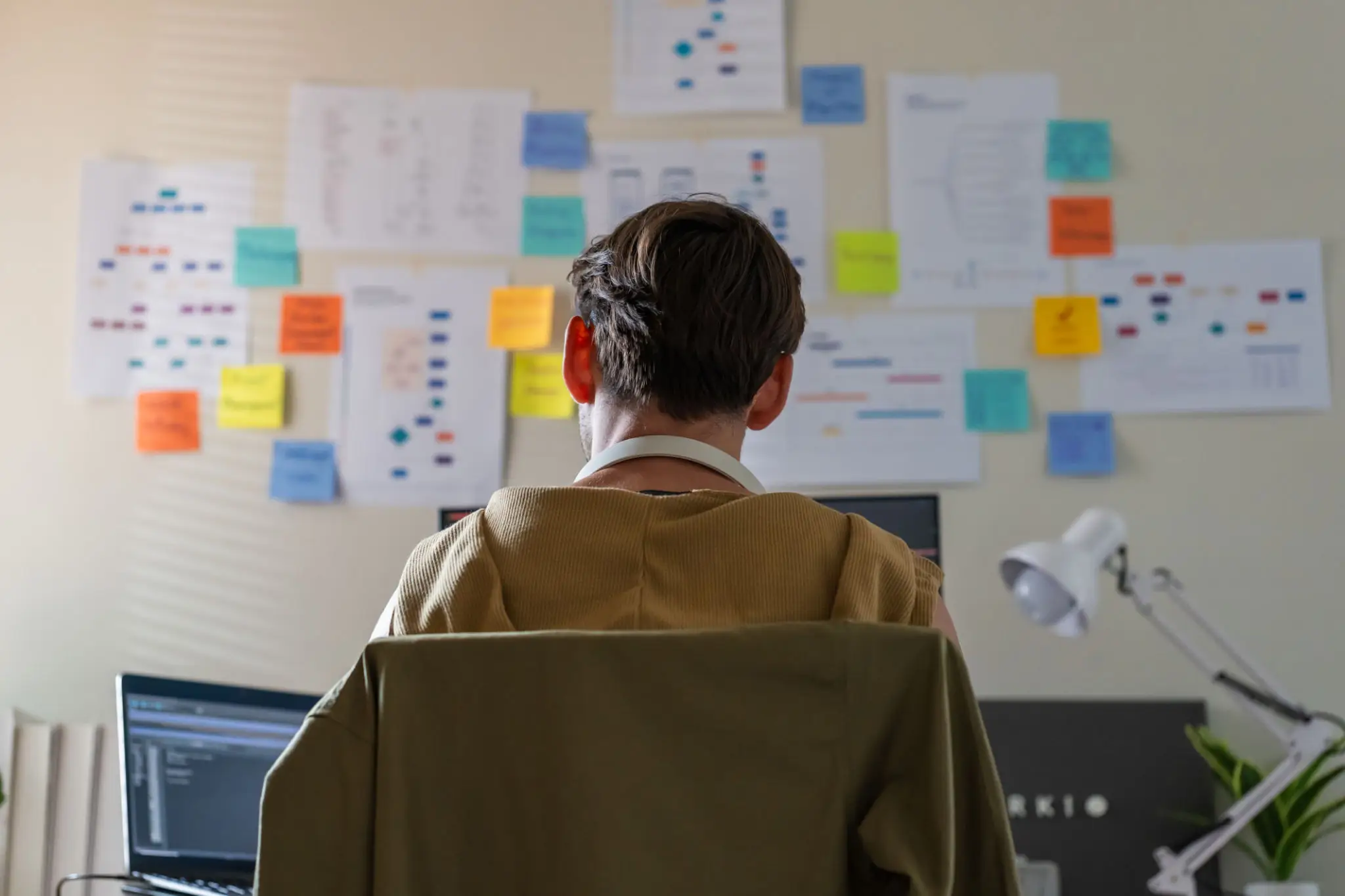 Focused Professional Working in Office with Mind Maps on Wall.