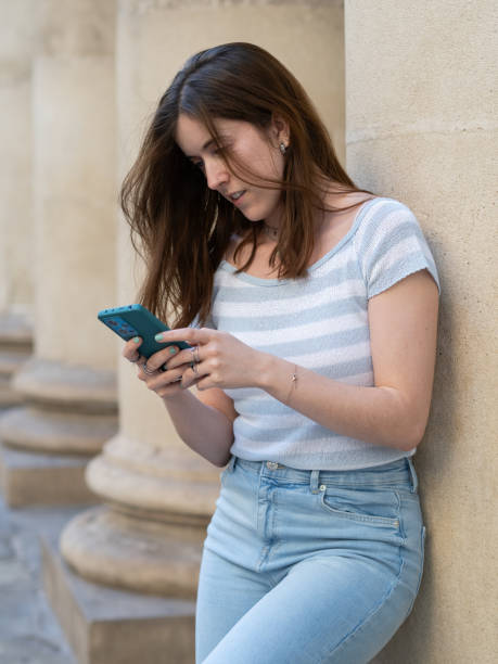 istock Young woman texting on her phone while leaning against a pillar 2175817745