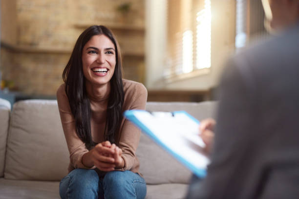 Happy woman talking to her therapist at home. Young happy woman communicating with a therapist during a home visit. mental wellbeing stock pictures, royalty-free photos & images