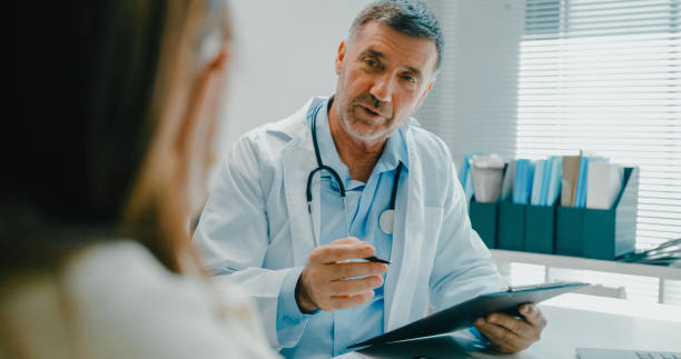 senior doctor in lab coat using digital tablet discusses medical test results with a patient in clinical office. medical health care. - bác sĩ hình ảnh sẵn có, bức ảnh & hình ảnh trả phí bản quyền một lần