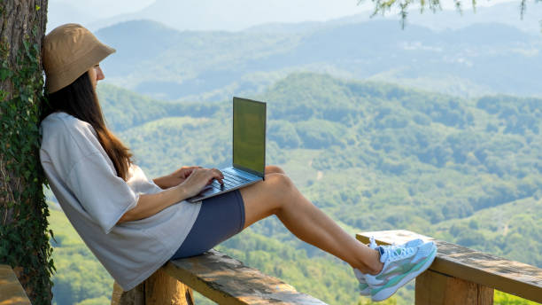 A young woman is working on a laptop in nature against the background of mountains stock photo