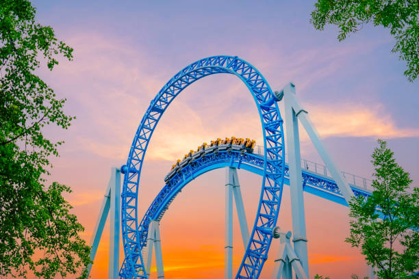 Roller coaster cart and people riding it goes through a loop upside down in green trees bushes city park sky sunset. Loop metal frame roller coaster in an amusement park Roller coaster cart and people riding it goes through a loop upside down in green trees bushes city park sky sunset. Loop metal frame roller coaster in an amusement park. rollercoaster stock pictures, royalty-free photos & images