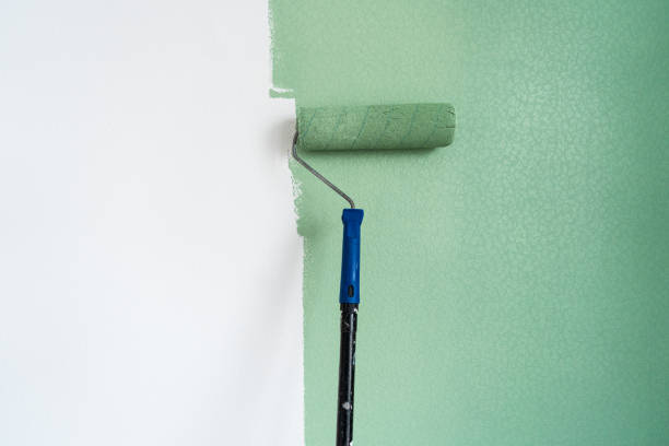 A paint roller with green paint at the wall