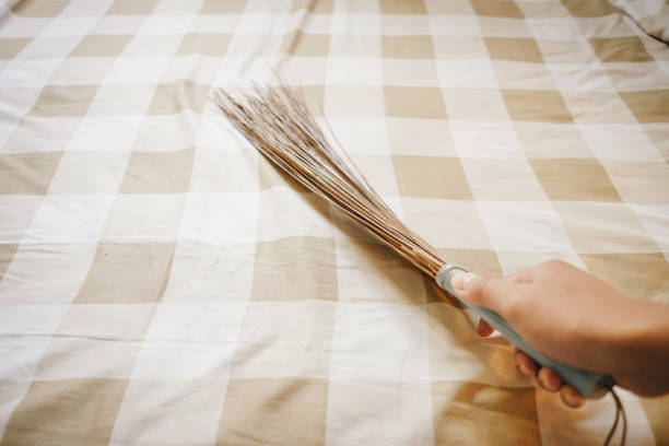 Hands cleaning bed sheet using broom stick after wake up from sleep inside bedroom