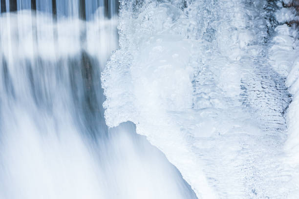 Icicles hang from the side of a waterfall, creating a stunning winter scene. The waterfall is located in a mountainous area, and the rocks are covered in ice. Hungary