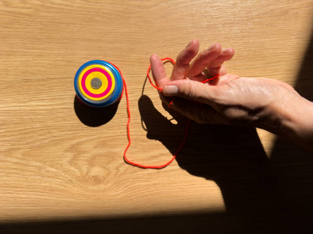 hand of unrecognizable person using a blue yo-yo toy to play.hard sunlight on parquet wood floor at home.games of skill and childhood classics. nostalgia and childishness.