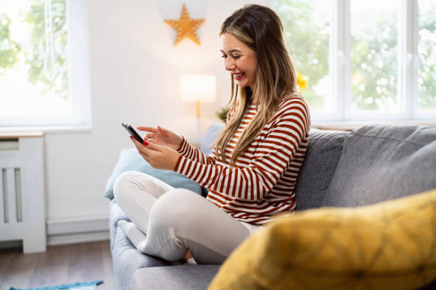 istock Young Caucasian woman using mobile phone for online purchases, while sitting on the sofa 2175856681