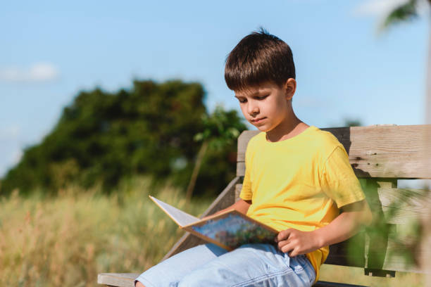 A child reads a book sitting on a bench in nature