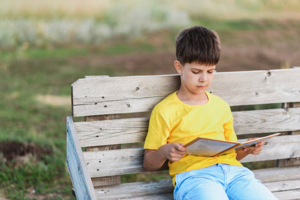 istock Cute boy reading a book sitting on a bench in nature 2175864494