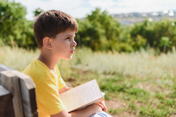 istock Cute boy reading a book sitting on a bench in nature 2175864817