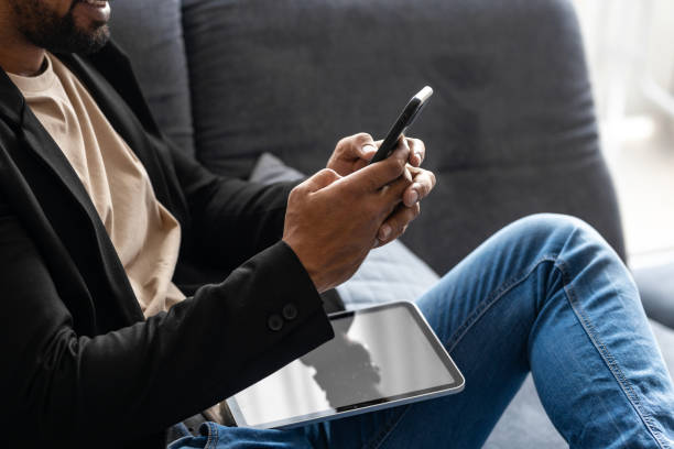 istock Black man using phone on couch in relaxed position while the tablet is in his lap 2175866550