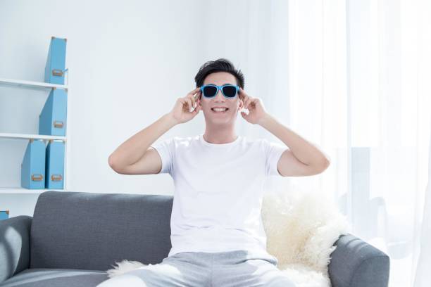 istock Young Asian man sitting on sofa wearing sunglasses and smiling 2175873376