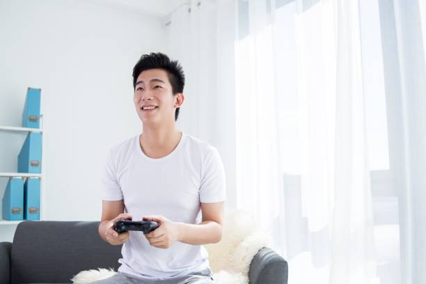 istock Young Asian man playing video games on the couch 2175873631