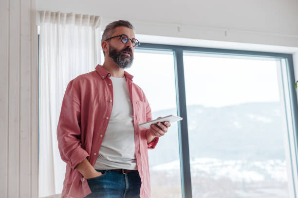 istock Man using smart thermostat, adjusting, lowering heating temperature at home. Smart home controlling roller blinds. 2175878537