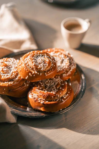 Traditional cinnamon buns topped with sugar on a rustic plate, paired with a cup of coffee, creating a cozy and inviting atmosphere. Photographed with selective focus.