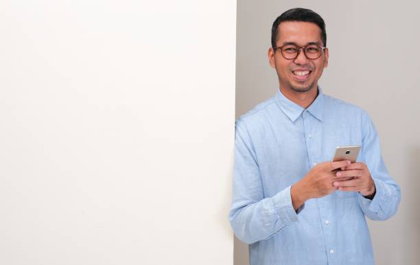 A man leaning on blank board holding mobile phone showing happy face