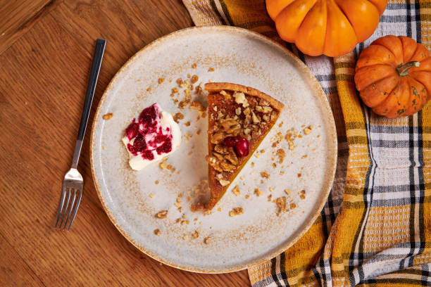 A slice of pumpkin pie with cream and cranberries rests on a ceramic plate on a wooden table