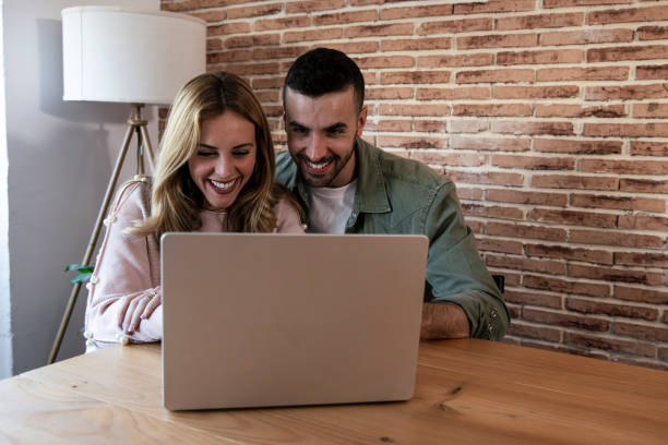 istock Happy man and woman using computer together while sitting in the living room. Young smiling couple connected on internet with device at their home. 2175902532