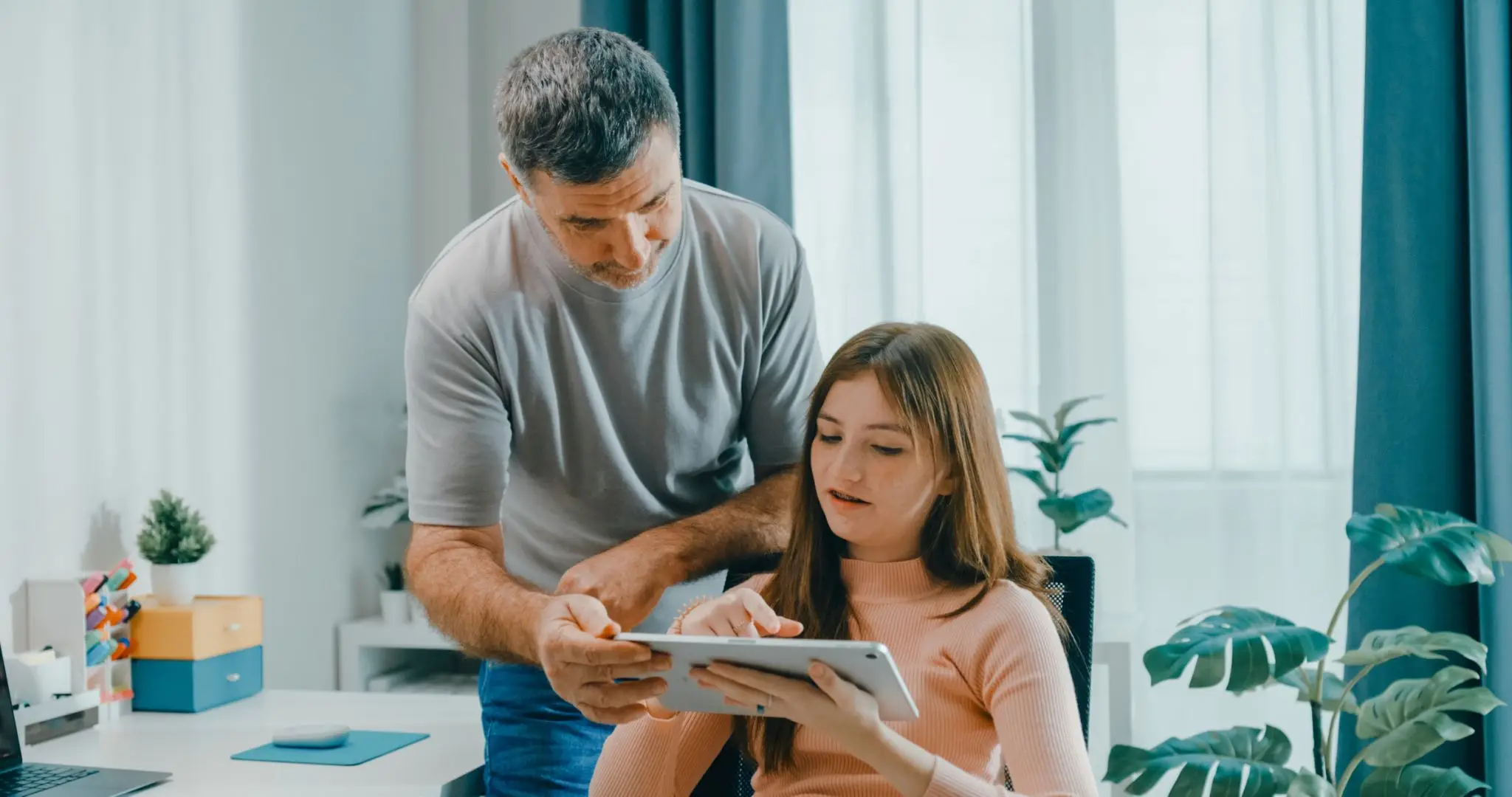Senior father assists his daughter with her work on digital tablet, promoting family bonding and technology use in learning at home. Lifestyle family.