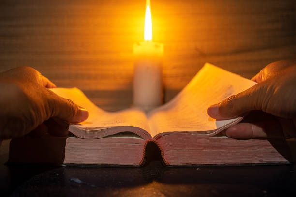 istock candle light with hands reading bible on wooden table in the night time. 2175920358