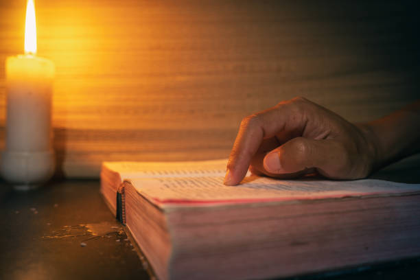 istock candle light with hands reading bible on wooden table in the night time. 2175920400