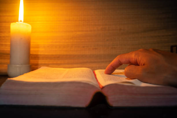 istock candle light with hands reading bible on wooden table in the night time. 2175920416