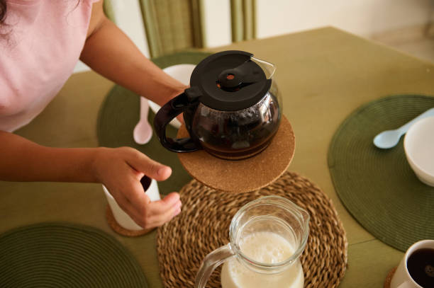 Person preparing coffee with milk at a dining table setting