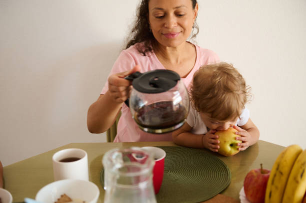 istock Mother enjoying coffee while child bites into an apple at table 2175927488