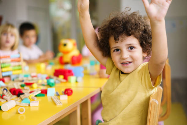 istock Boy with raised hands is sitting at a table in a kindergarten 2175931126